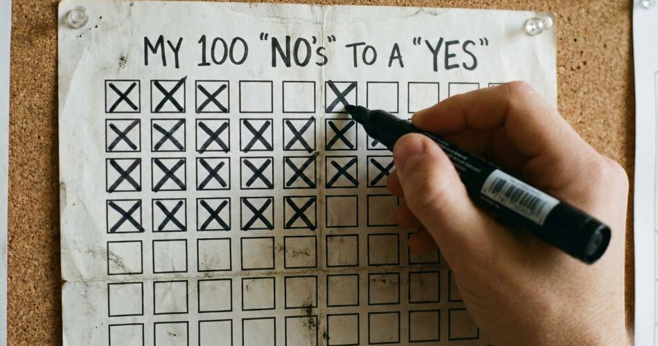 High-performance Real Estate Strategies. A close-up of a 100-Box Grid on a piece of paper, with a hand crossing out a box to track rejections, gamifying the prospecting process.