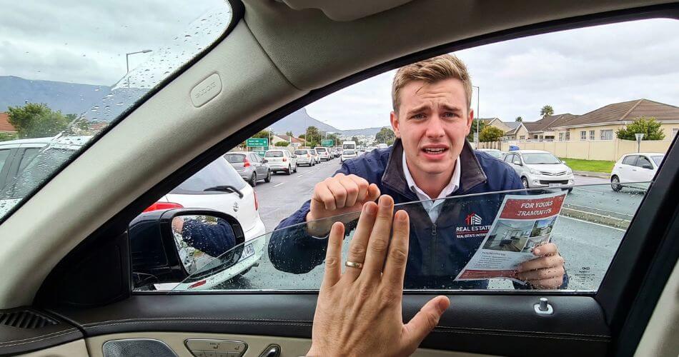 Mentoring Intern Estate Agents. Driver inside a car refusing a flyer from an estate agent intern at a traffic light.